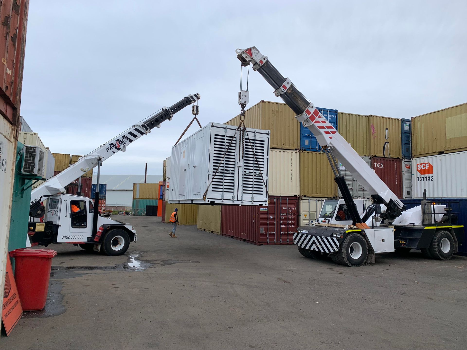 Two cranes are lifting a container in a parking lot