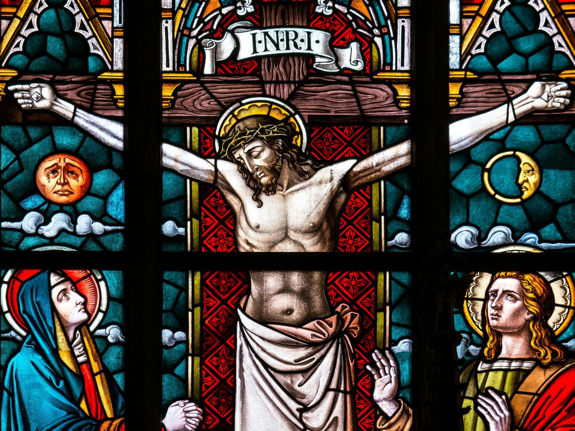 Stained glass window: Jesus on the cross, flanked by figures, a sun and moon.