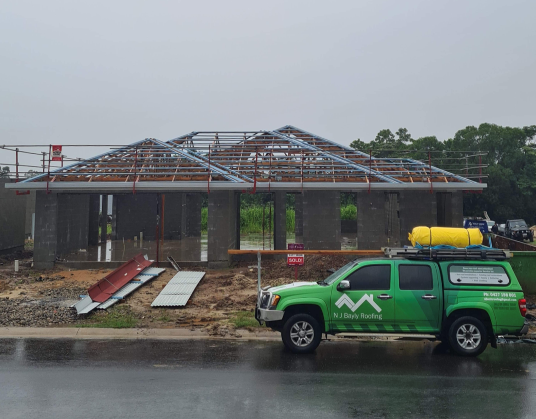 A green truck is parked in front of a house under construction.