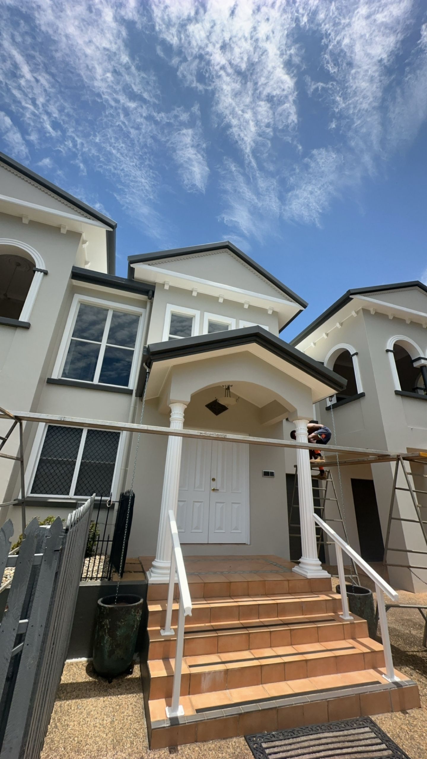 A large white house with stairs and a blue sky in the background.