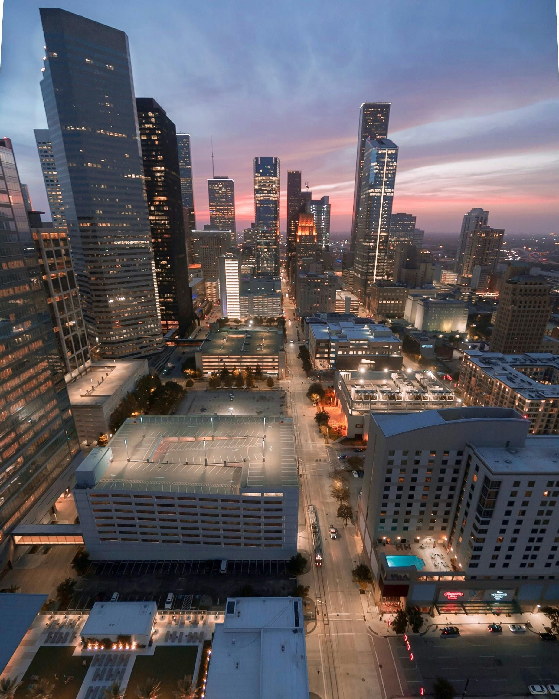 Downtown cityscape at dusk, lit buildings and streetlights reflecting on a long street.