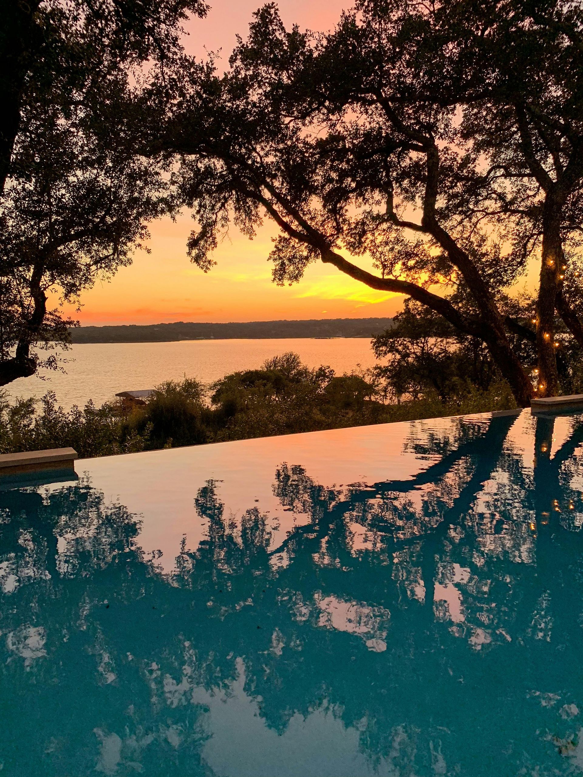 Sunset over water reflected in a pool; silhouetted trees frame the sky.