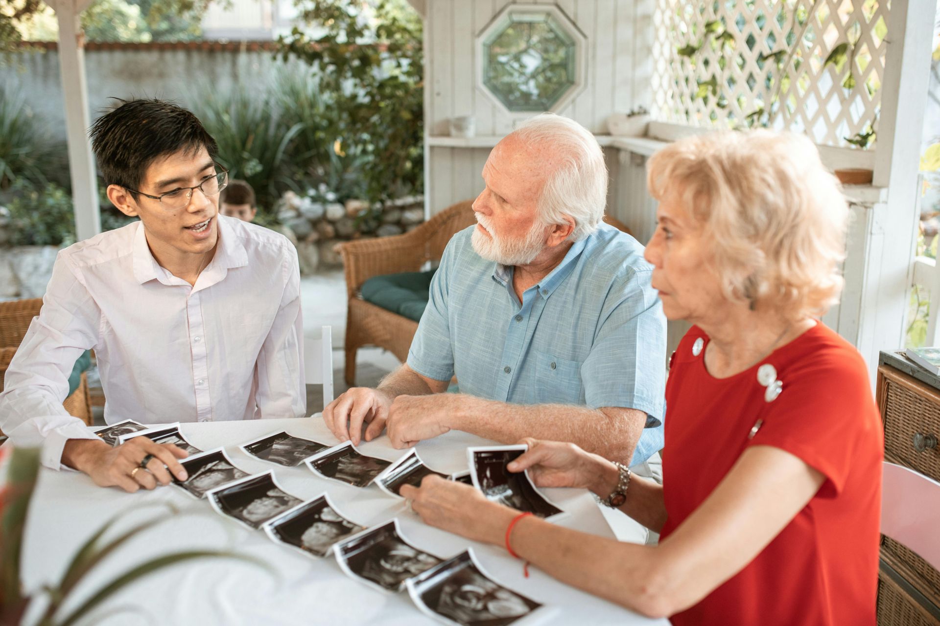 Man showing ultrasound photos to older couple at a table on a porch.