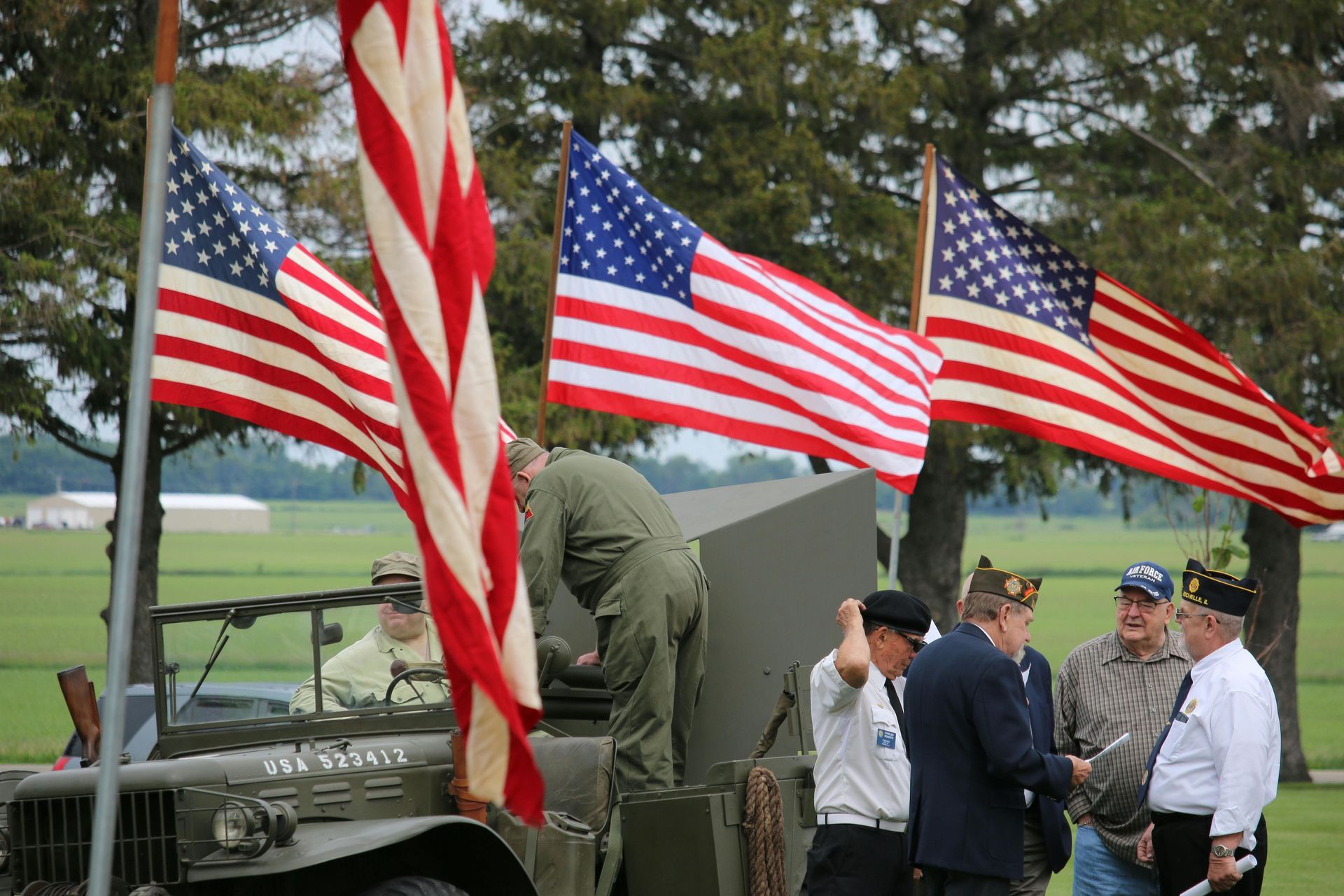 American flags wave near veterans at an outdoor ceremony.