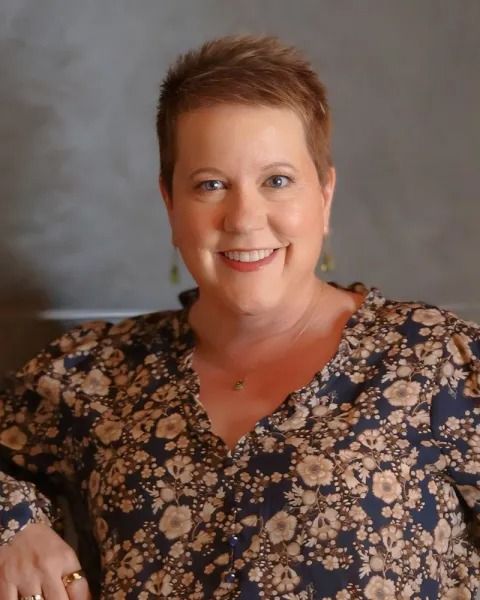 Woman with short brown hair, smiling, wearing a floral blouse.
