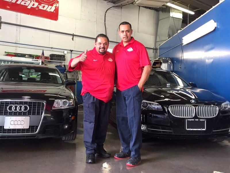 Two men are posing for a picture in front of a bmw and an audi
