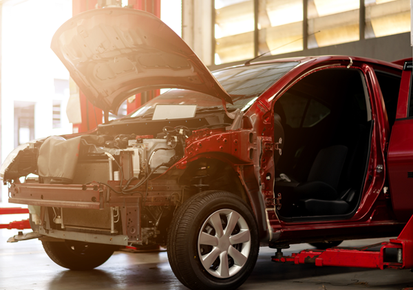 A red car is being repaired in a garage with the hood open.