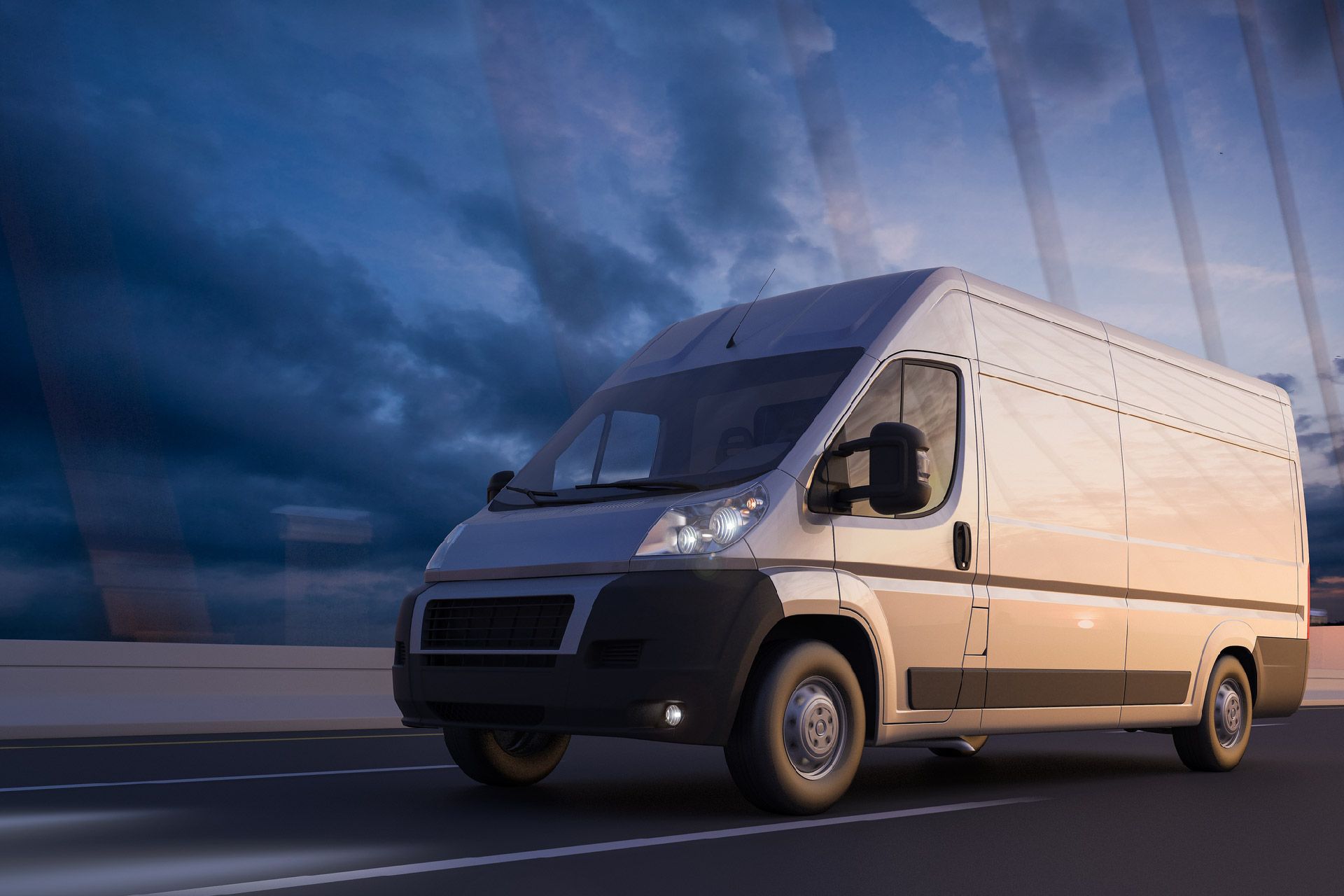 Furgoneta de reparto blanca circulando por una carretera contra un cielo nublado al anochecer.