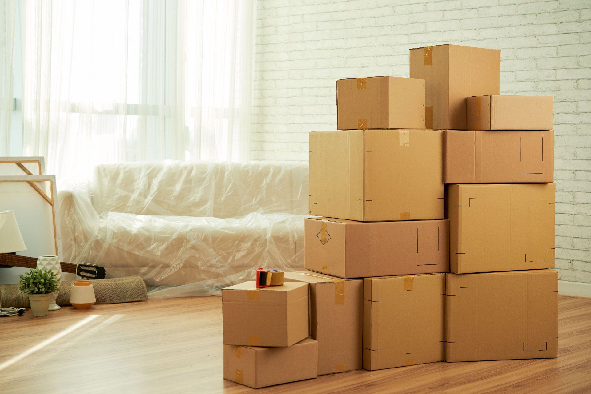Pila de cajas de mudanza en una habitación prácticamente vacía, con un sofá cubierto con film plástico visible al fondo.