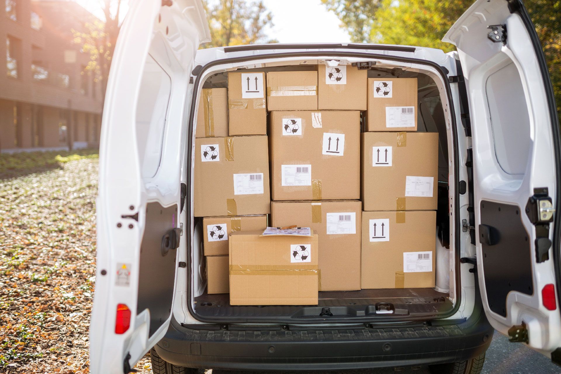 Furgoneta de reparto blanca con las puertas abiertas llena de cajas de cartón apiladas.