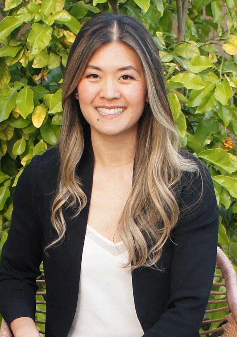 A woman in a black jacket is sitting on a bench in front of a tree.