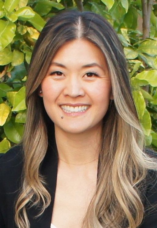 A woman with long hair is smiling and wearing a black jacket.