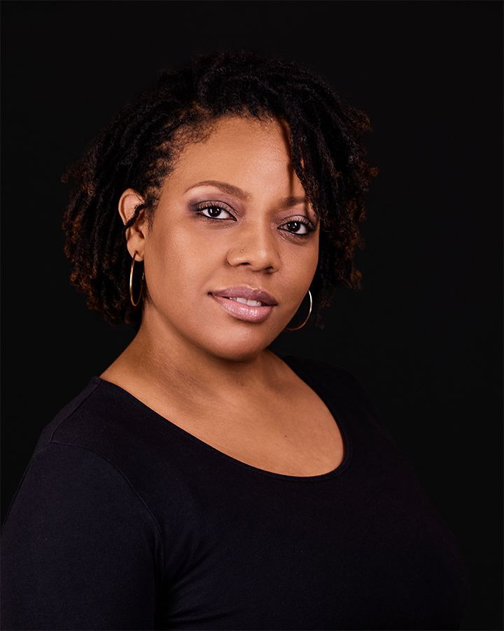 Woman with dark skin, wearing a black top, smiles gently against a black background.