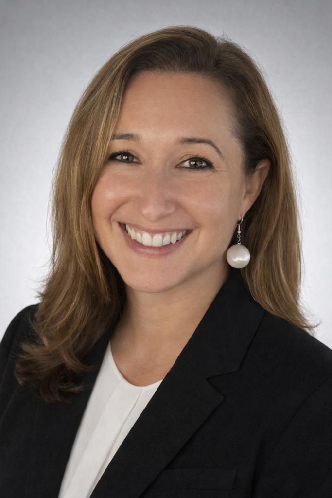 Christa Forero Woman smiling, wearing a black blazer and white shirt, pearl earrings.
