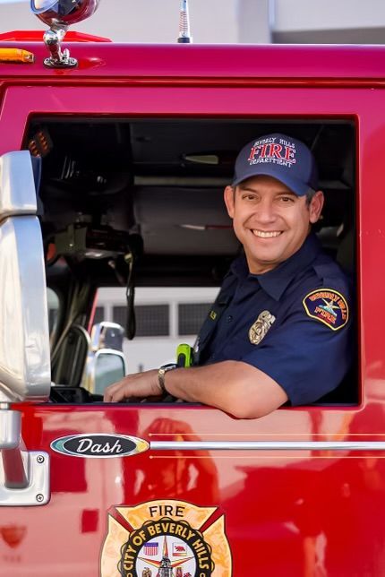 Manny Paul Rosales Firefighter in uniform smiling inside red fire truck, City of Beverly Hills.