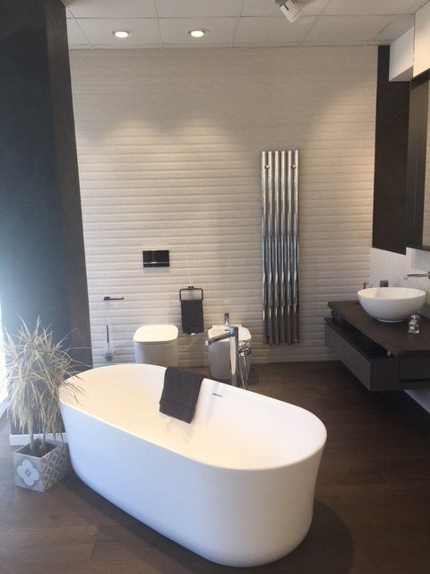 Bagno moderno con vasca freestanding bianca, pavimento in legno scuro, lavabo a parete e termoarredo.