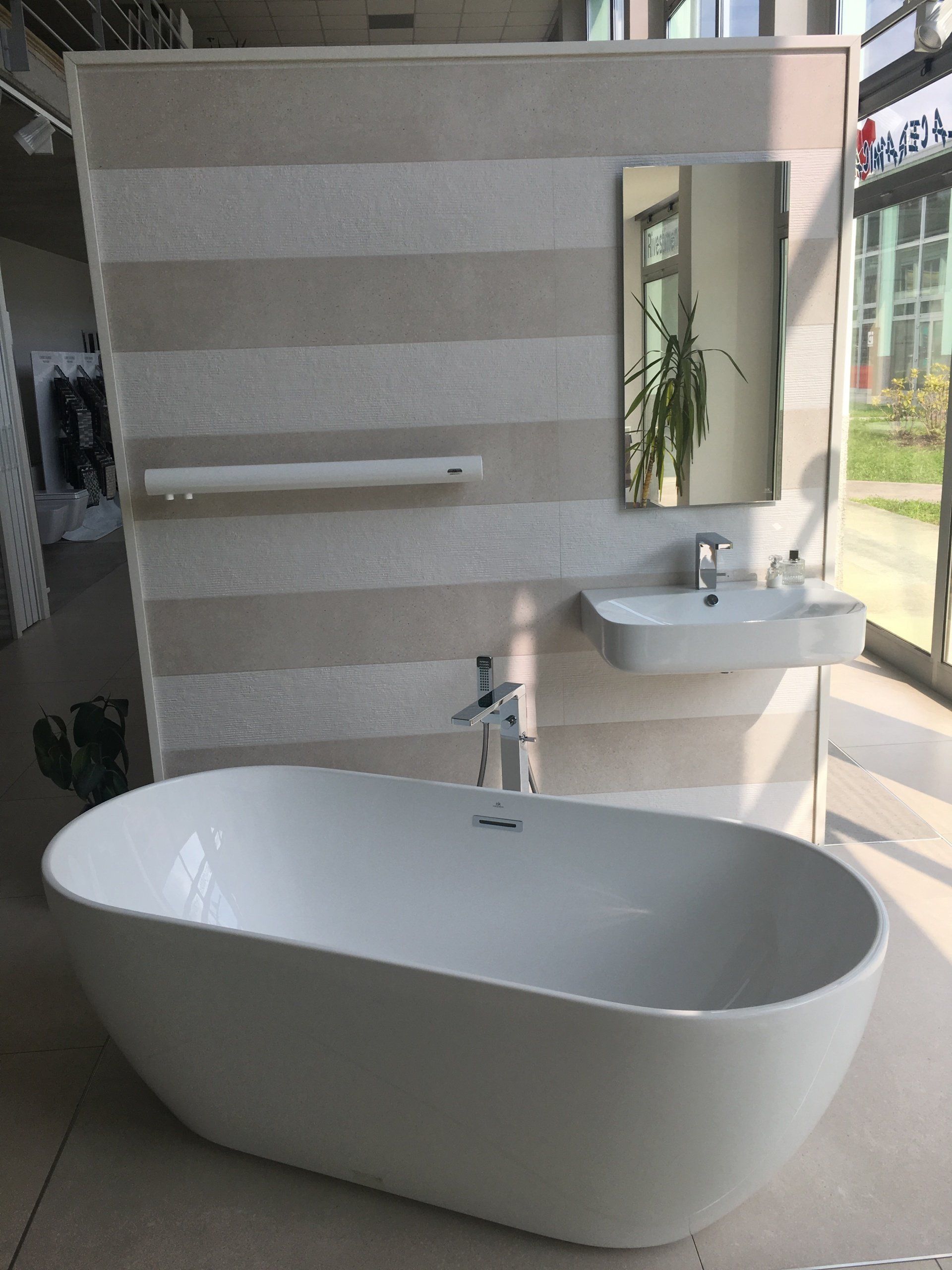 Bagno moderno con vasca bianca freestanding, lavabo a parete e specchio su una parete piastrellata a righe.