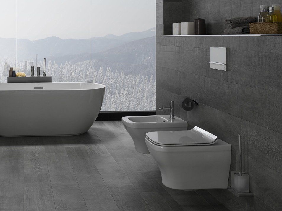 Bagno moderno di colore grigio con vasca freestanding, WC sospeso, bidet e ampia finestra con vista sulle montagne innevate.
