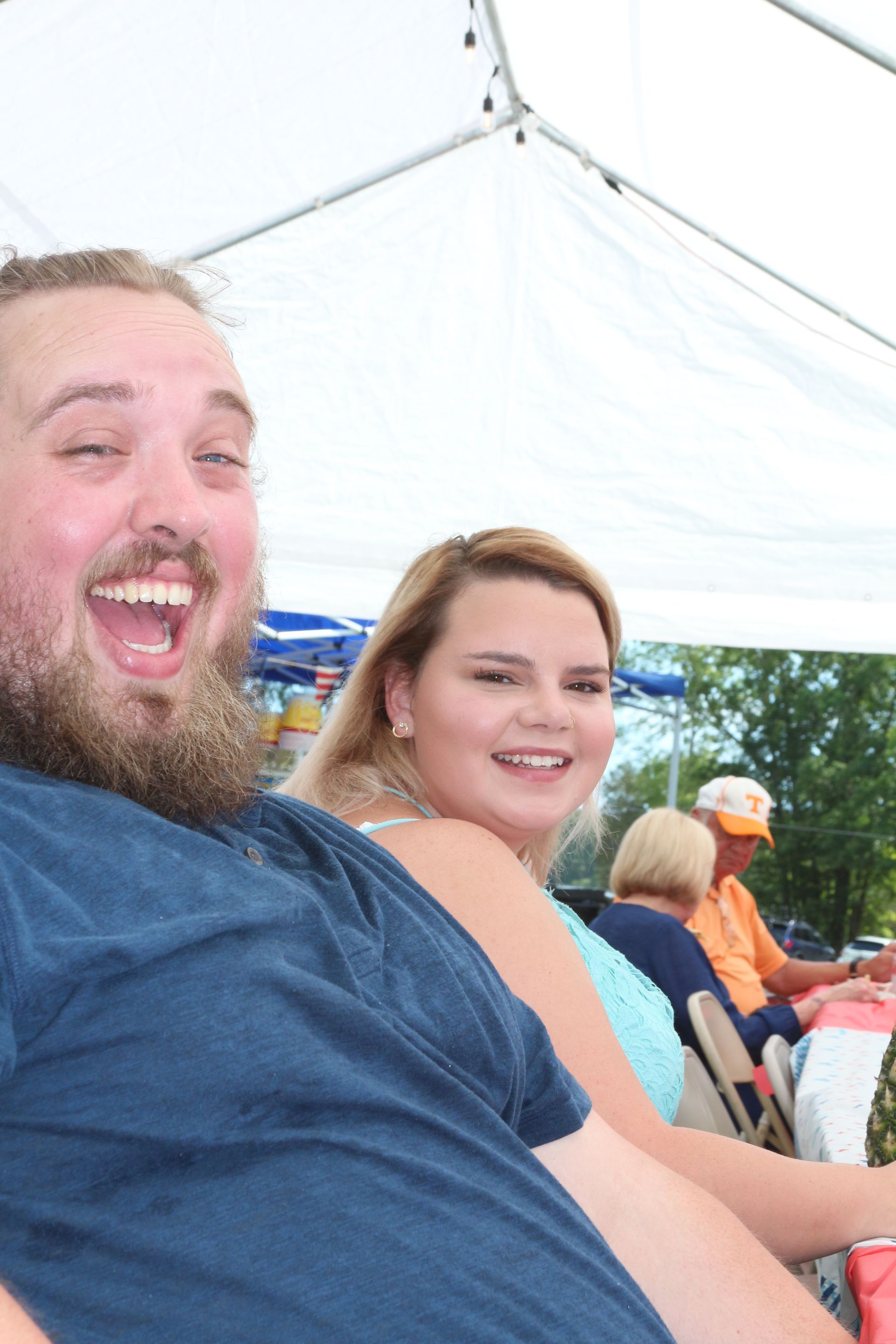 A man and a woman are sitting under a tent and smiling.