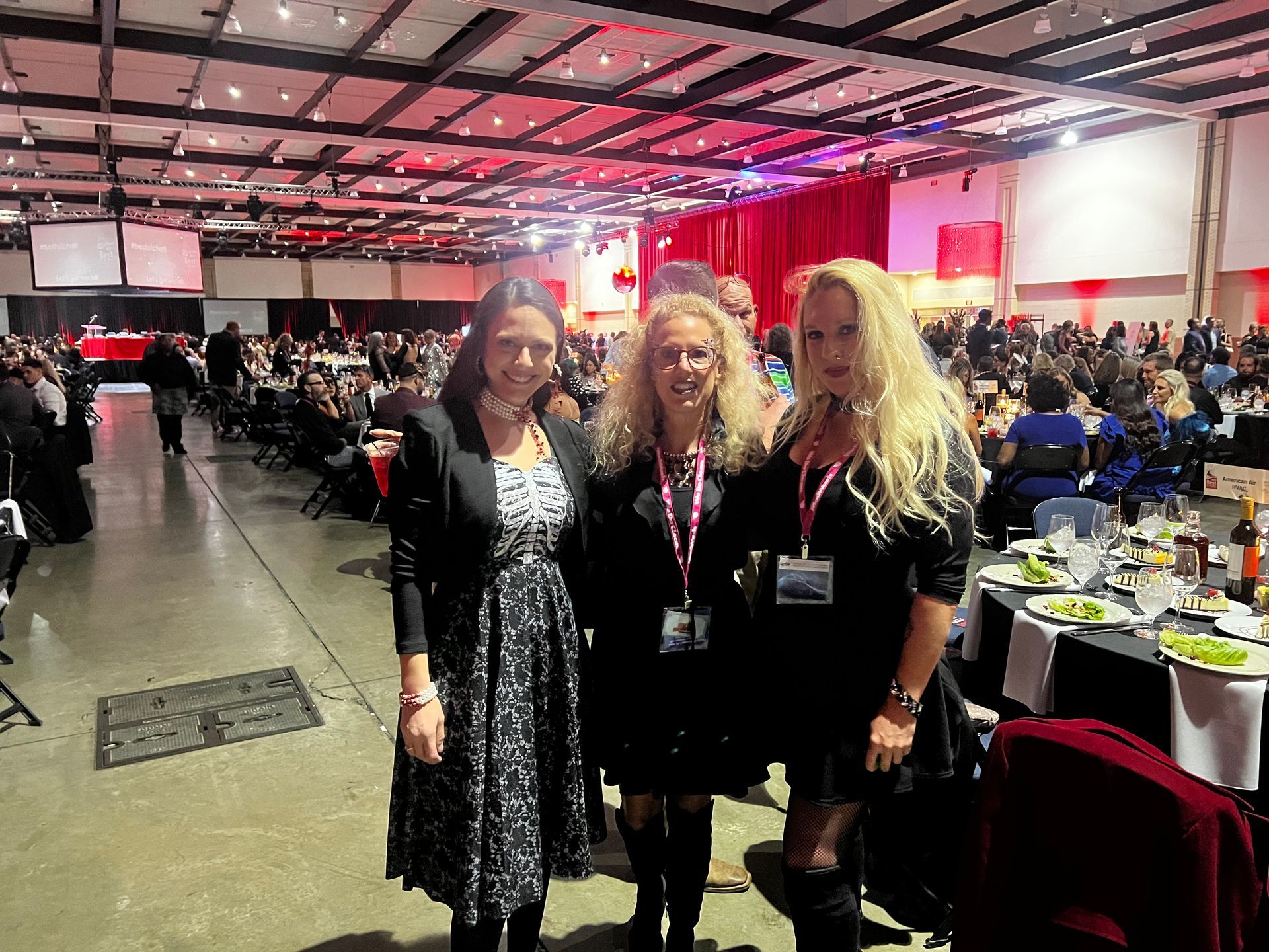 Three women are posing for a picture in a large room with tables and chairs.