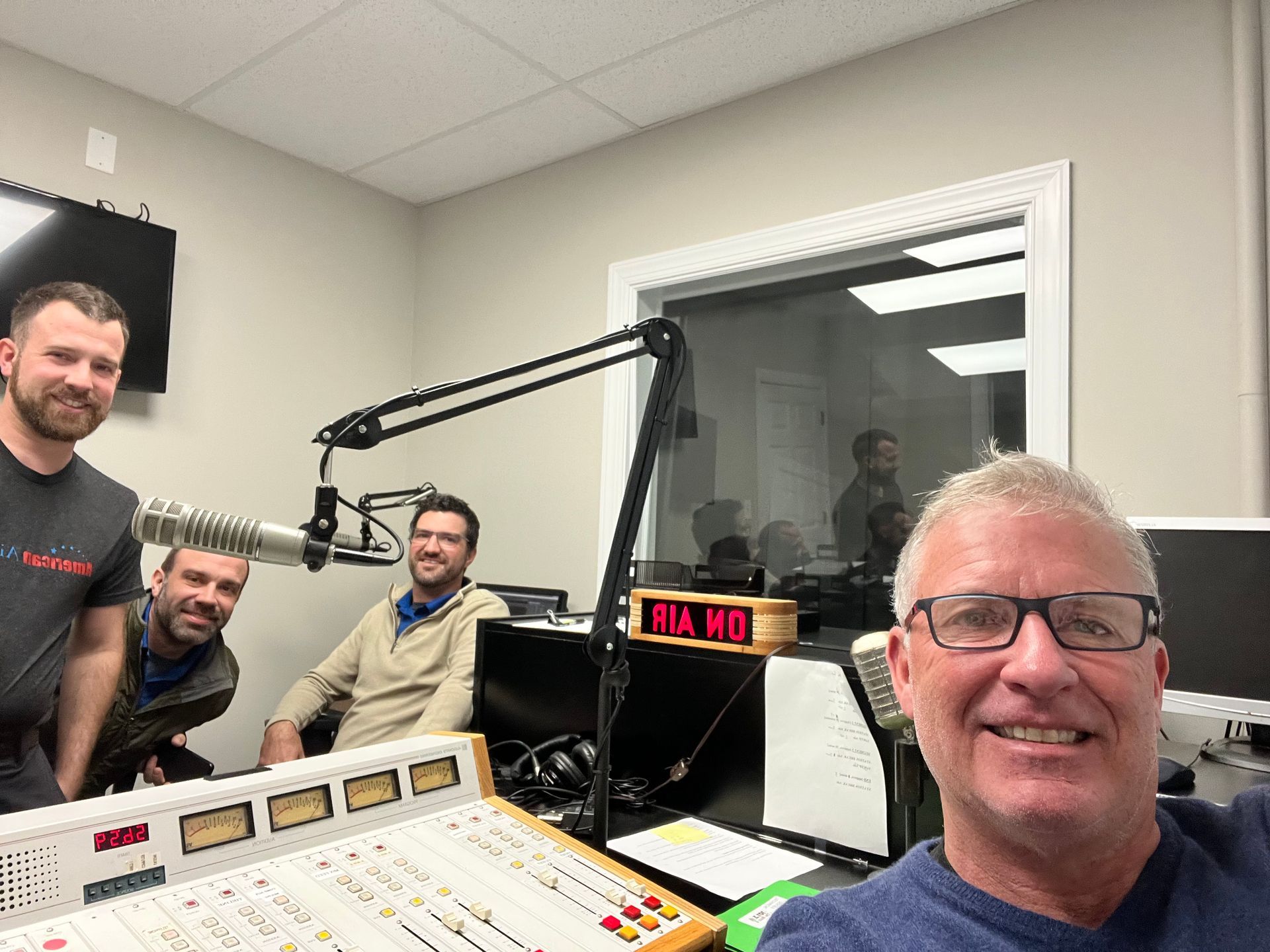 A group of men are standing in front of a microphone in a radio studio.