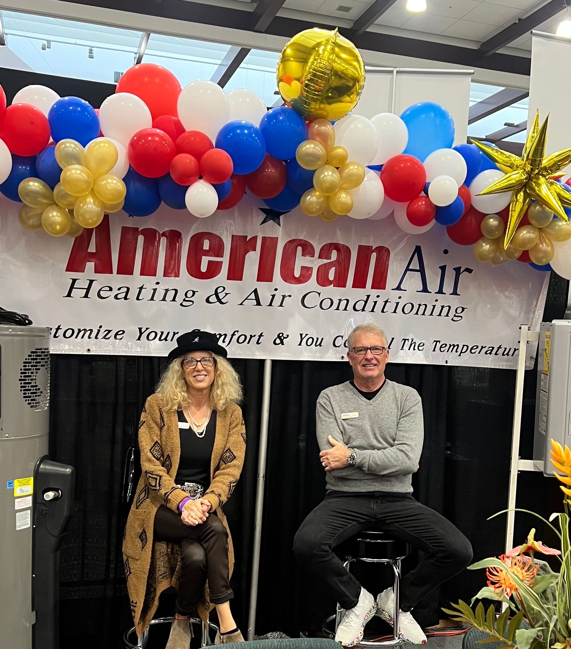 A man and a woman are sitting in front of a sign for american air heating and air conditioning.