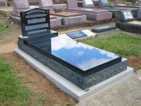 A polished black granite headstone and tomb cover set on a light concrete base in a cemetery.