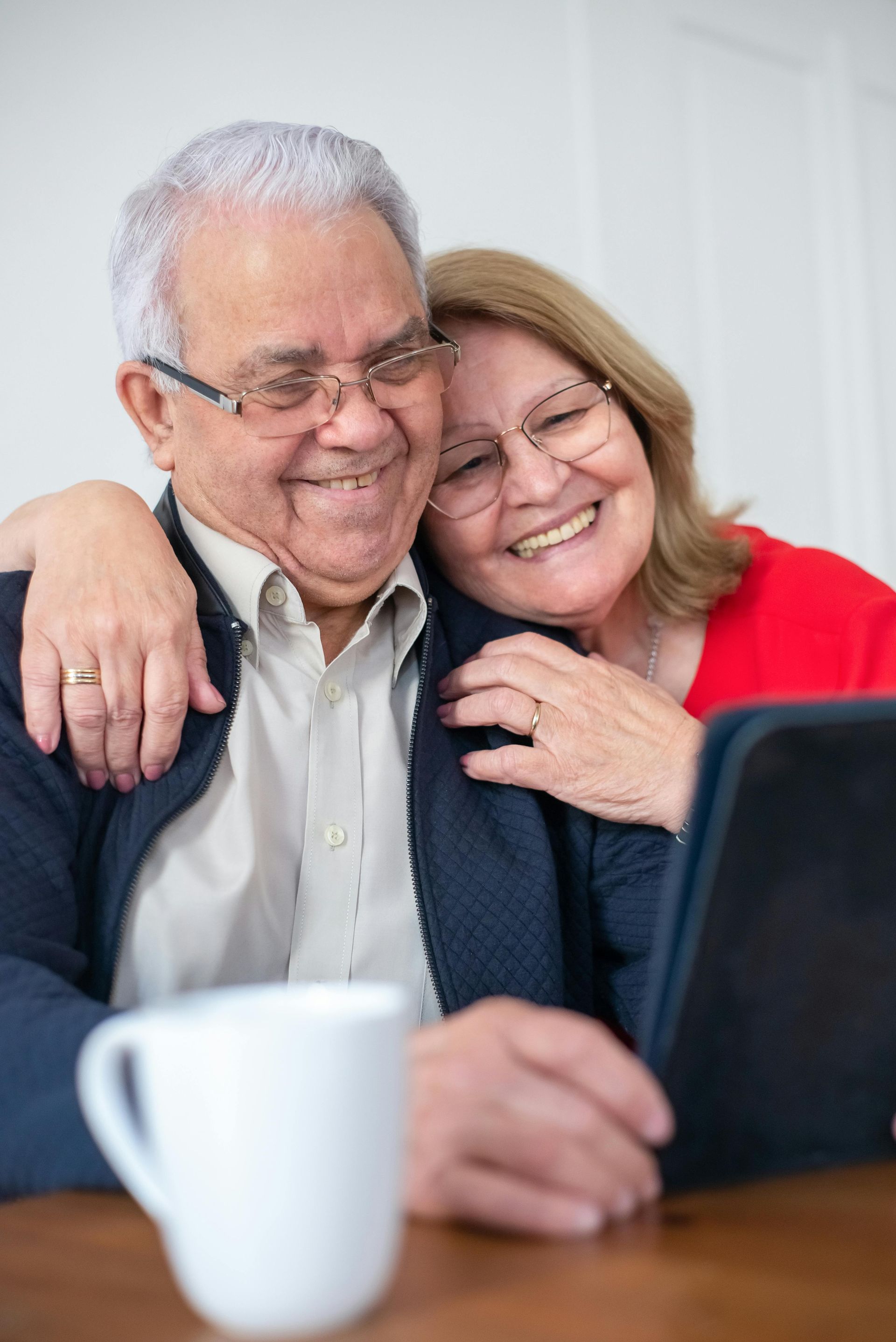 An elderly couple is sitting on a couch looking at a tablet.