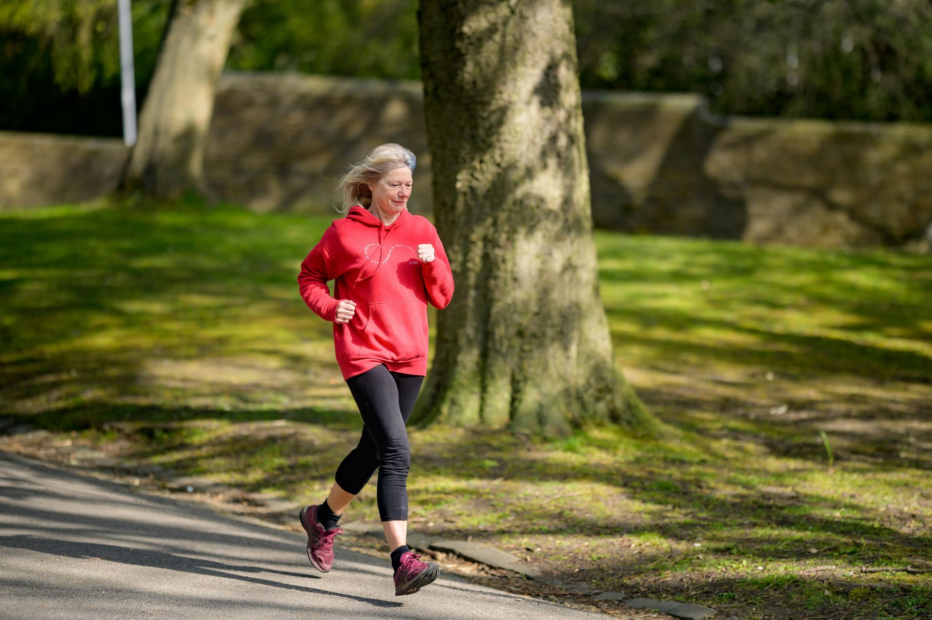 A woman in a red hoodie is running down a road in a park.