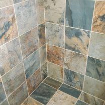 Corner of a shower with multi-colored square tiles, gray, blue, and brown hues. White grout lines.