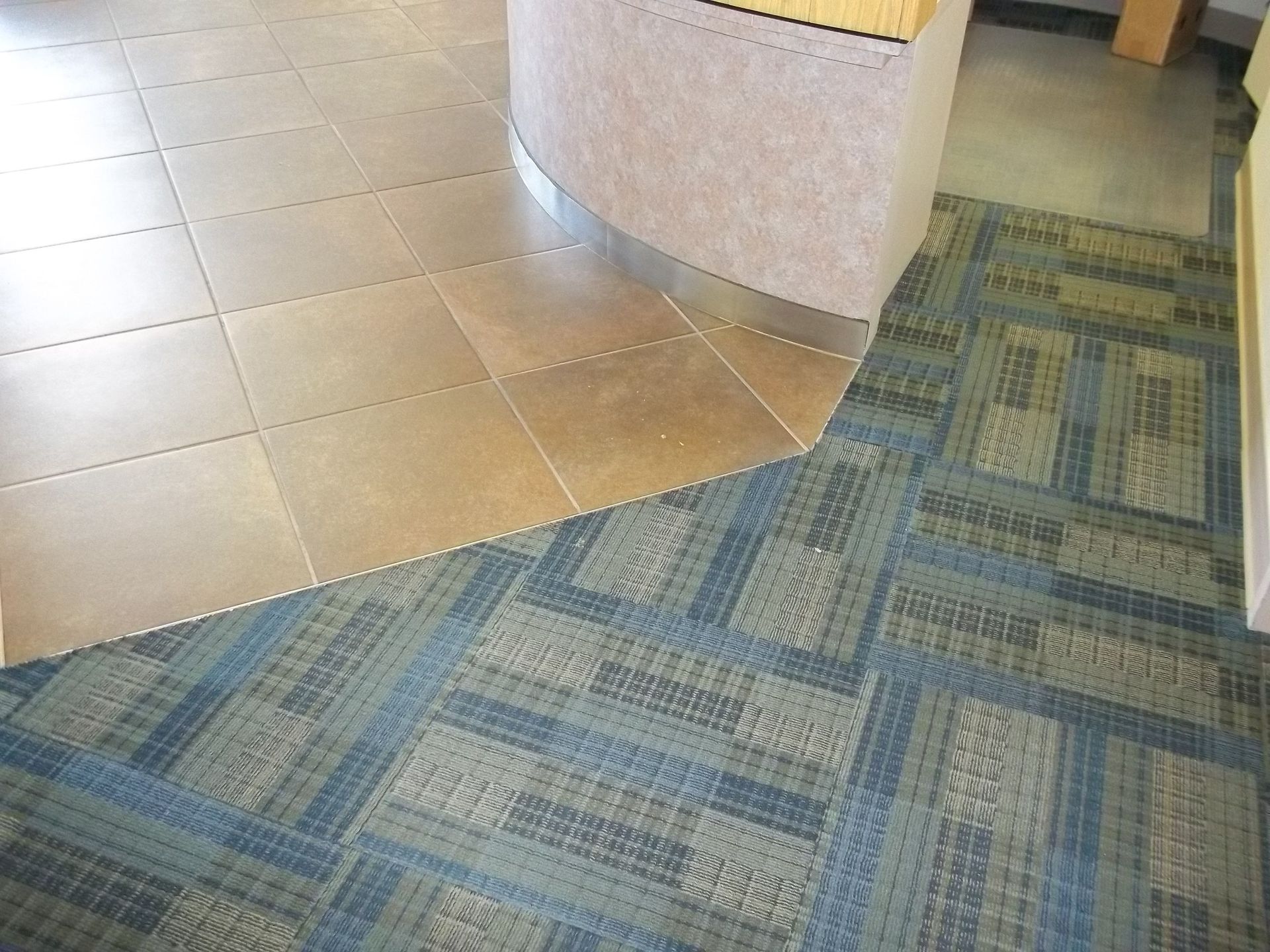 Floor with metallic tile and blue patterned carpet meeting around a curved wall.