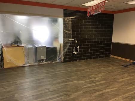 Interior space under renovation, with black brick wall, plastic sheeting, exposed utilities, and gray wood-look flooring.