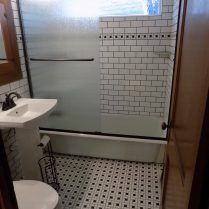 Bathroom with white subway tile shower, pedestal sink, black and white floor tiles.