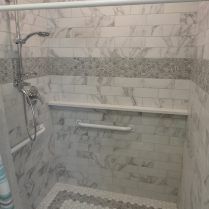 Accessible shower with white marble-like tile, grab bar, showerhead, and built-in shelf.