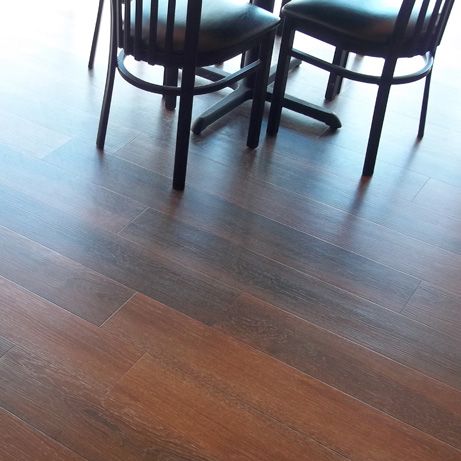 Brown wood-look floor with a table and black chairs in a brightly lit setting.