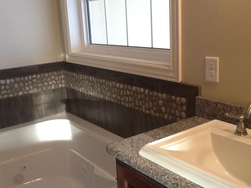 Bathroom with bathtub, sink, and window. Brown and pebble tile border. Beige walls, white fixtures, and granite countertop.