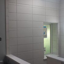 White tiled wall with opening to a green-lit room. A white ledge is in the foreground.
