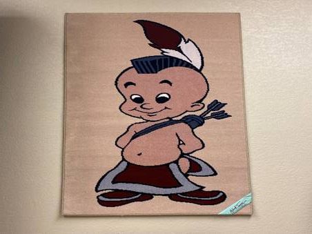 Cartoon Native American figure with a mohawk, holding arrows, on a beige background.