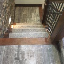 Staircase with wood and carpet treads, leading downward. Walls are stone and wood, with a metal railing on the right.
