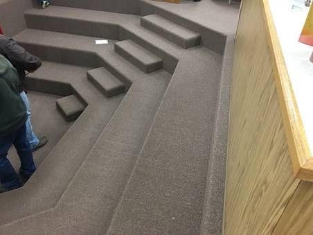 Carpeted tiered seating with people, next to a wooden wall.