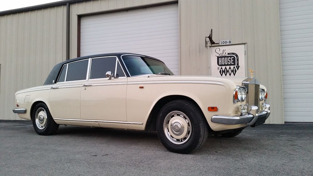 Classic cream Rolls-Royce parked outside a garage door in an industrial lot