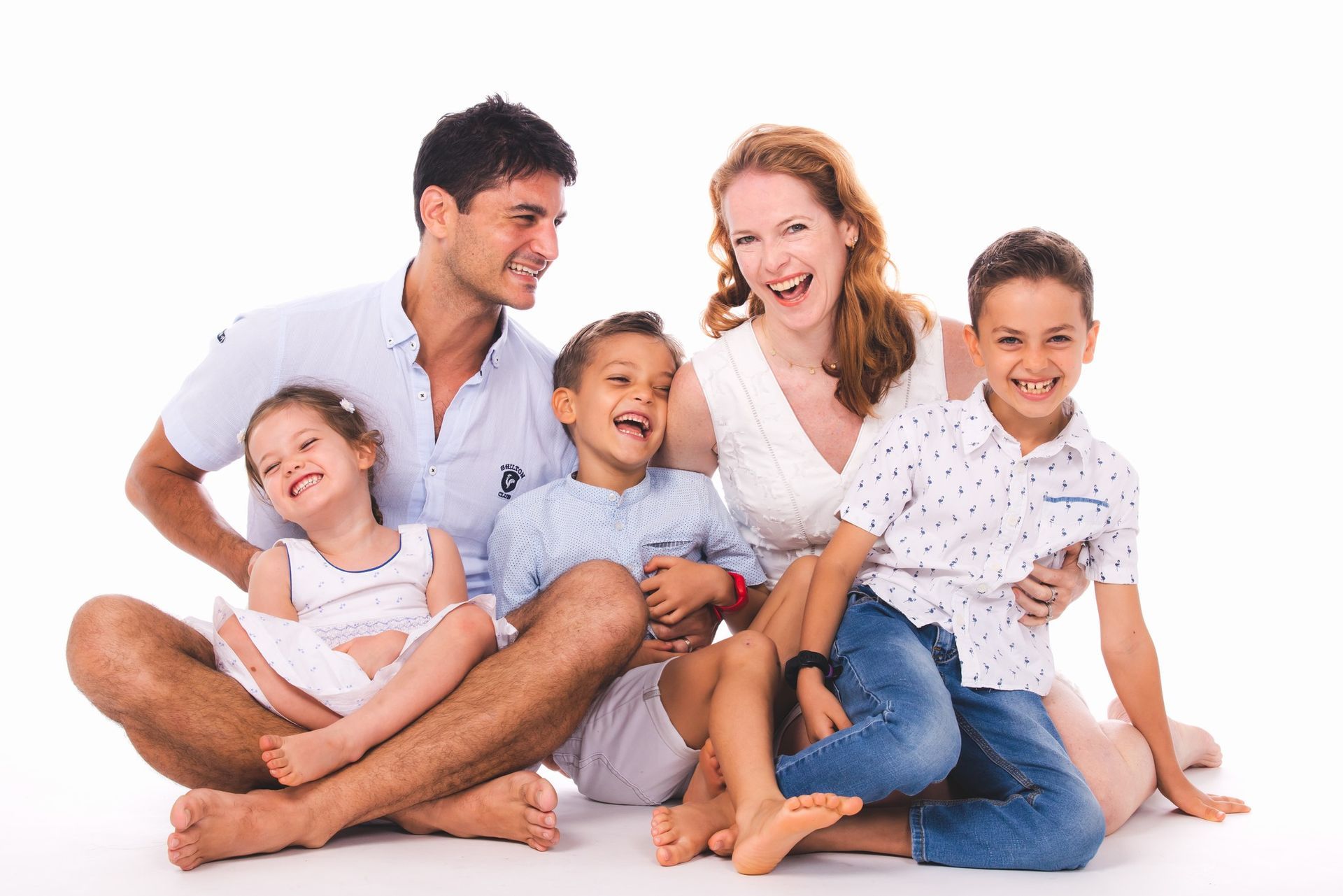 A family of five sitting together on a white background, all smiling and laughing.