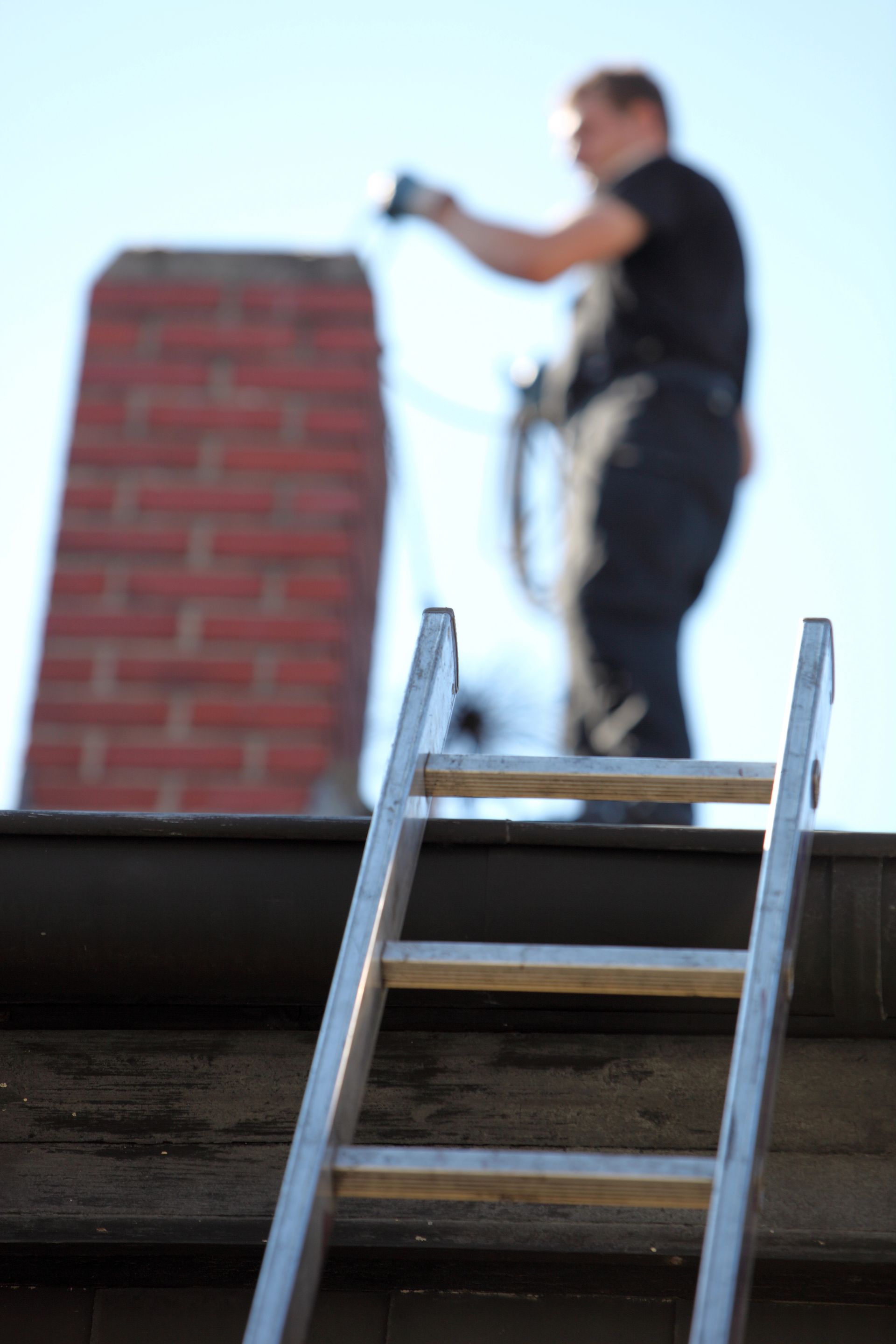 A man is standing on a roof with a ladder in front of him