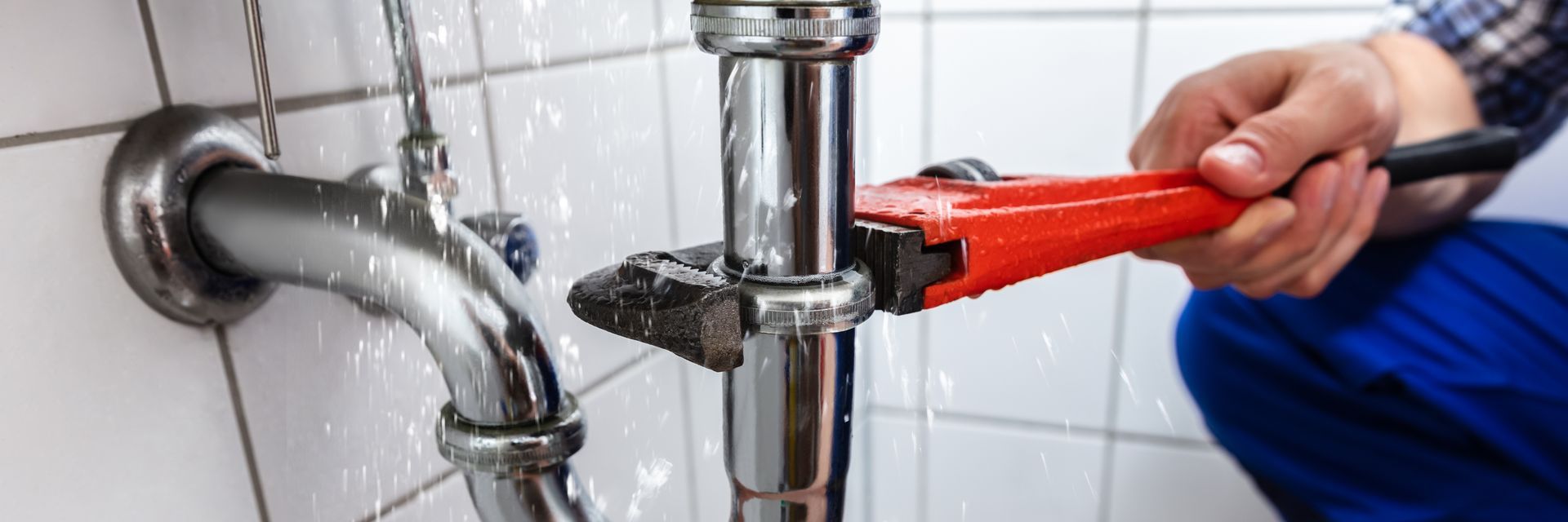 A plumber is fixing a leaking pipe with a wrench.