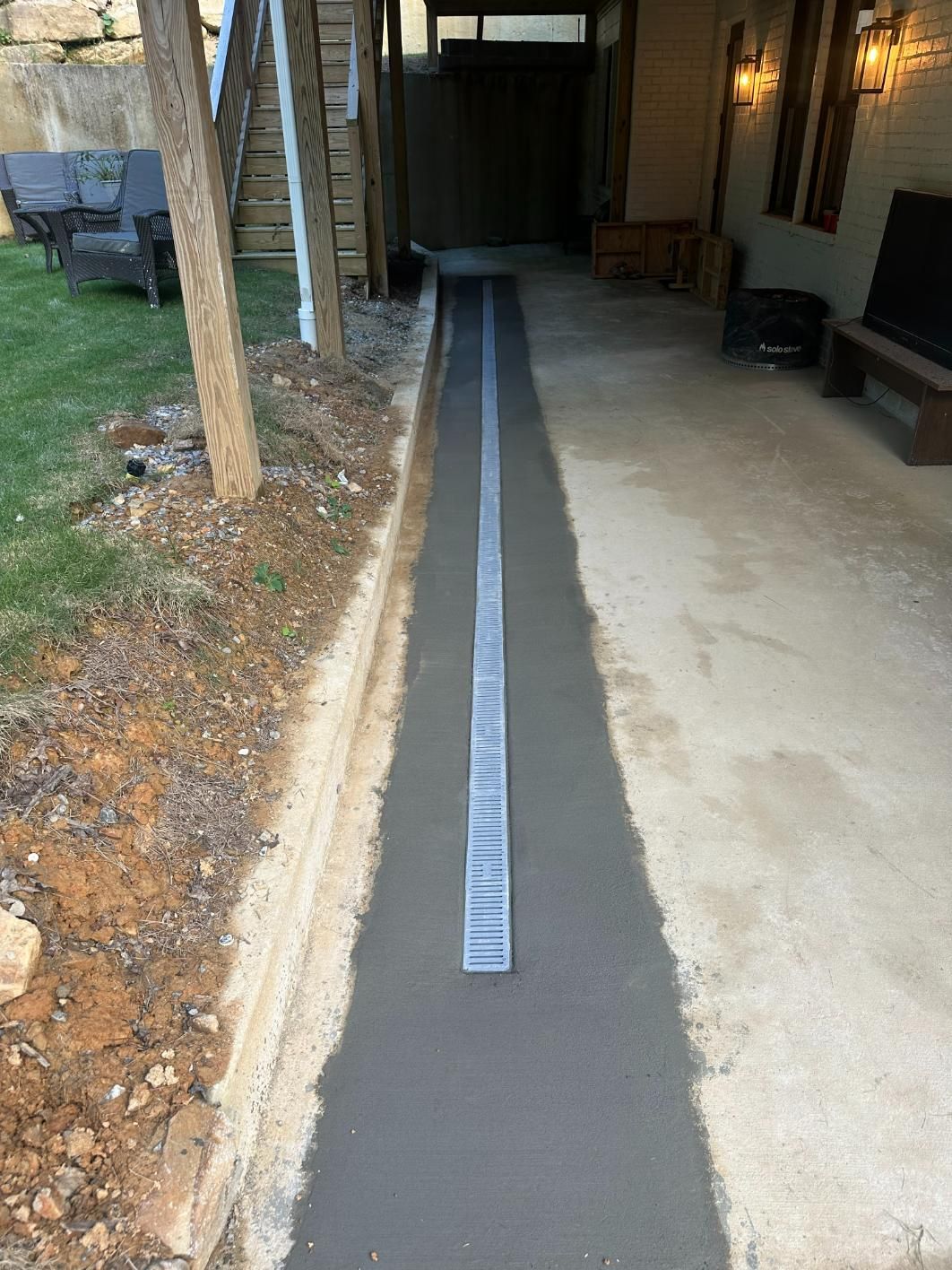 Narrow concrete trench with a metal grate, next to grass and a building.