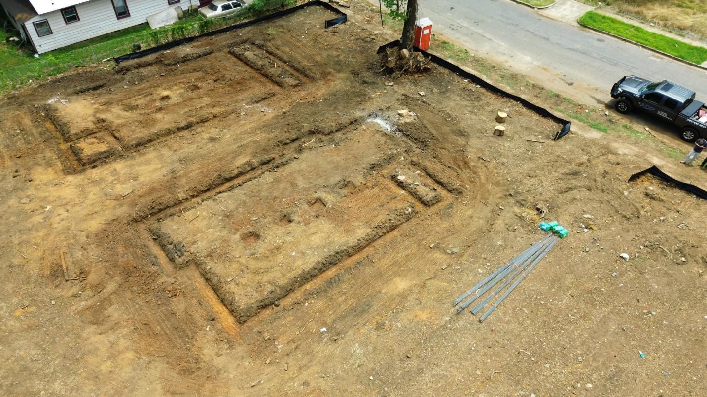 Aerial view of a construction site with excavated foundations, dirt, and a nearby road.