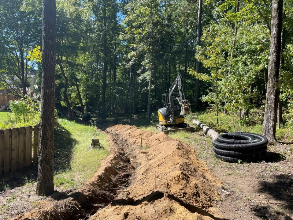 Trench dug in a wooded area with a small excavator and corrugated pipes.