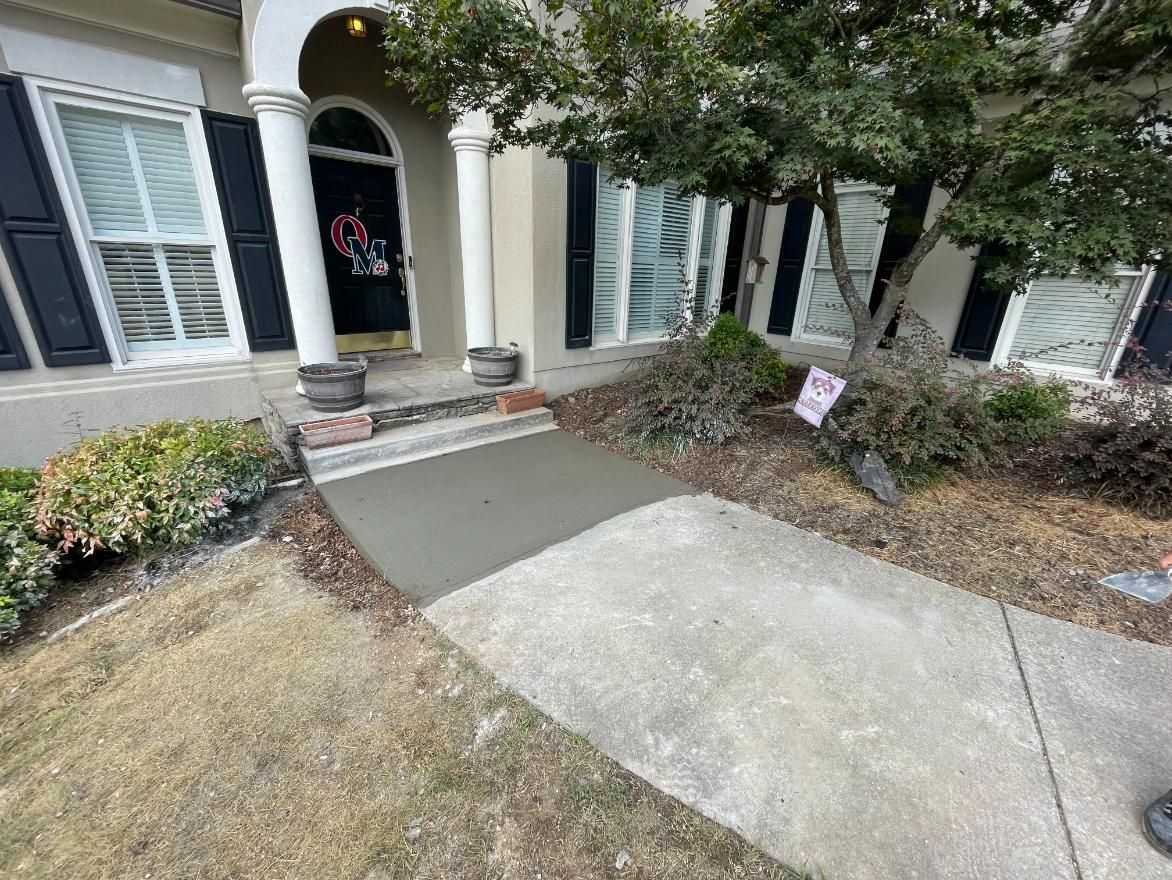 Cement pathway leads to a house entrance with a new concrete patch. Dry grass surrounds.
