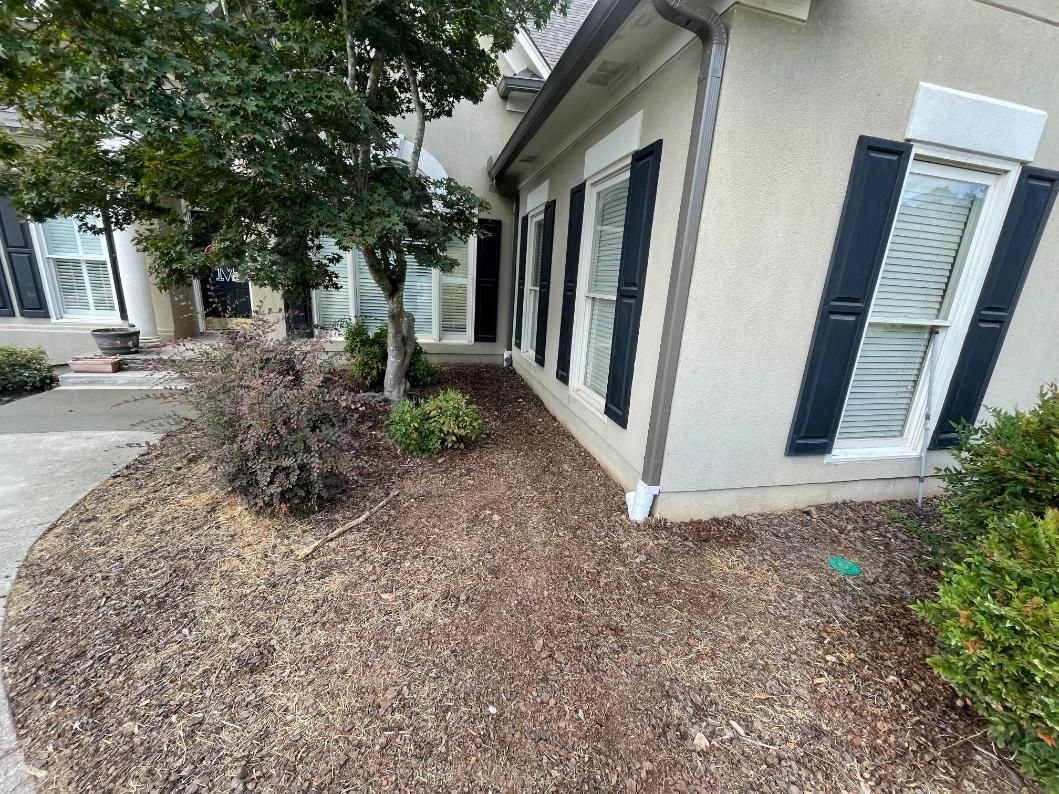 Exterior of a house with mulch landscaping, dark shutters, and a sidewalk.