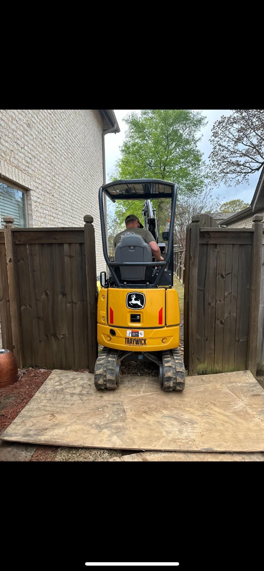 Yellow John Deere mini excavator between two wooden fences, a person inside.